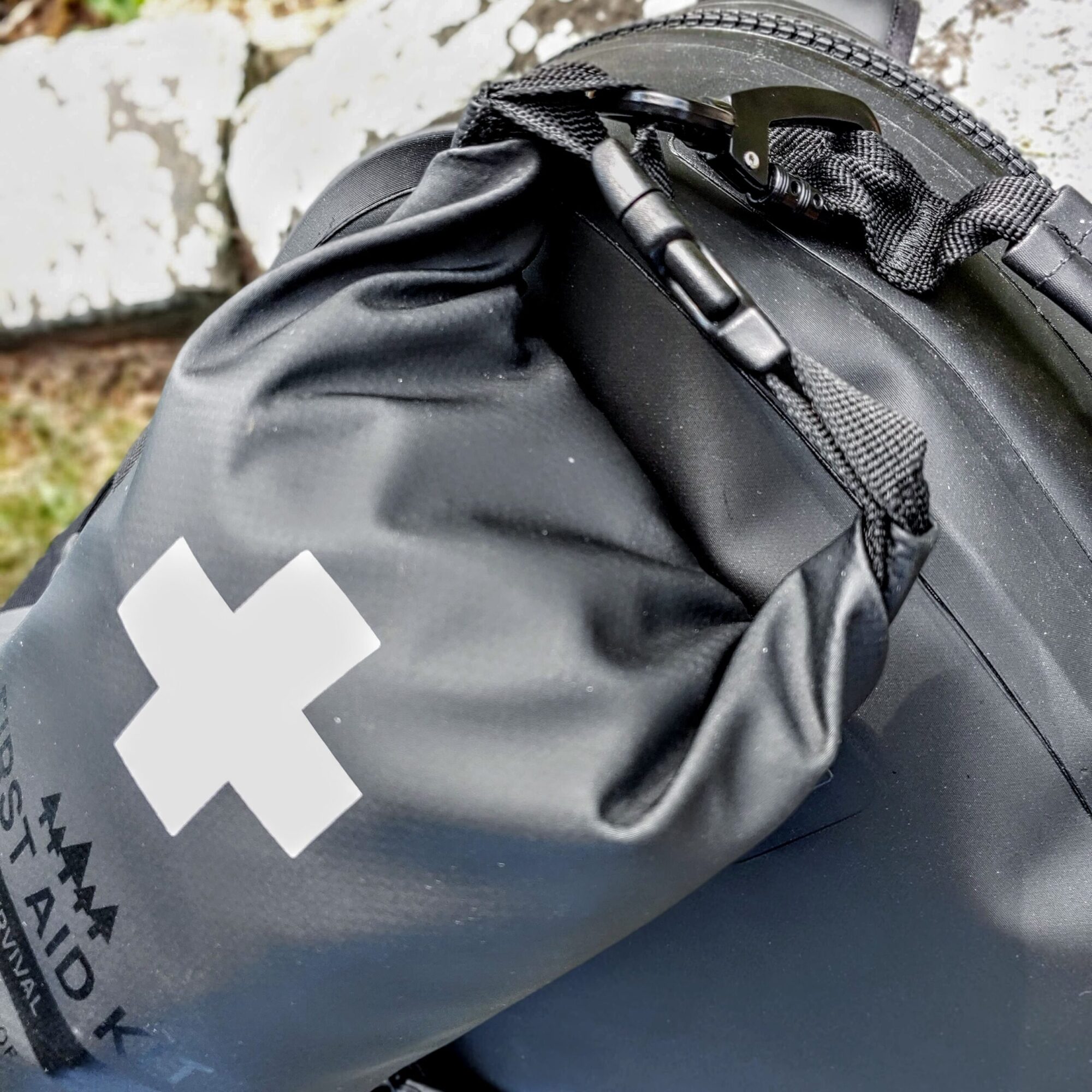 Breakwater Supply Stealth Black Survival Kit with metal carabiner clipped to Fogland Waterproof Backpack